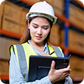A warehouse worker wearing a construction hat checks items off a list on her clipboard. 